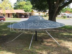 an umbrella sitting on top of a metal stand in the grass next to a tree