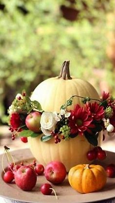 an arrangement of flowers and fruit on a plate outside in the fall season, with pumpkins and apples