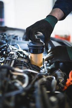 a man is working on the engine of a car while wearing gloves and holding a coffee cup