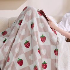 a person laying on a couch under a blanket with strawberries on it and reading a book