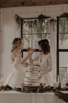 two women standing next to each other in front of a cake