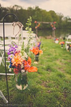 an outdoor ceremony setup with flowers in mason jars and white chairs on the sidelines