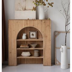 a wooden shelf with vases and other items on it next to a white vase