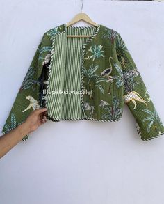 a person holding onto a green jacket with dinosaurs on it