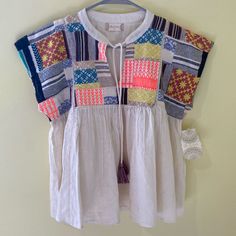 a white shirt with multicolored patchwork on it hanging from a hanger