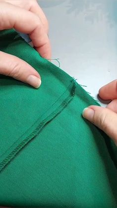 two hands are working on a green piece of fabric that is being sewn together