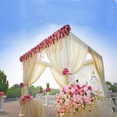 an outdoor wedding setup with pink flowers and white draping on the side of it