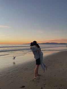 two people hugging on the beach at sunset