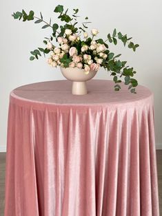 a vase with flowers on top of a pink table cloth covered round dining room table