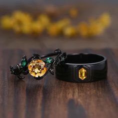 two black rings with yellow and green stones on them sitting on top of a wooden table