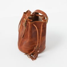 The English Tan Dublin Bucket Bag is an heirloom-quality bag handmade of full-grain leather. English Tan Dublin is a thick, waxed leather with a smooth grain and dramatic pull-up, produced by the Horween tannery in Chicago. Classic Satchel Bucket Bag With Smooth Grain, Timeless Bucket Bag With Leather Lining, Cognac Smooth Grain Satchel Bucket Bag, Classic Leather Satchel Bucket Bag, Timeless Leather Bucket Bag With Leather Handles, Classic Bridle Leather Bag With Waxed Finish, Classic Leather Bucket Bag In Cognac, Cognac Bridle Leather Bag With Leather Backing, Timeless Leather Bucket Bag With Leather Lining