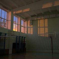 an indoor basketball court with net in the middle and sun shining through windows behind it