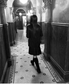 a woman walking down a long hallway in black and white with her back to the camera