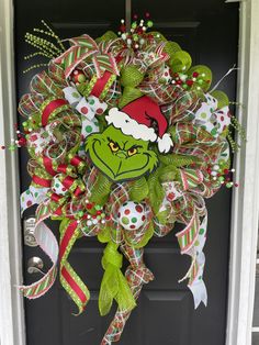 a christmas wreath with the grin face on it's front door decorated with green and red ribbons