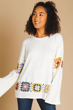 a woman wearing a white sweater with colorful flowers on the side and bell sleeve sleeves