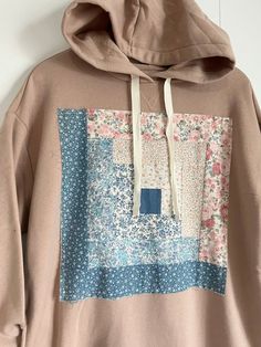 a brown hoodie with blue and pink patchwork on the front, hanging up against a white wall