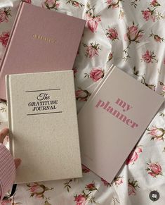 two pink books sitting on top of a bed next to a person's hand