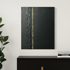 a black and gold painting hanging on the wall next to a plant in a white room