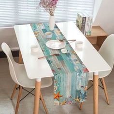 the table is set with two white chairs and a blue wooden table runner that has seashells on it