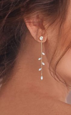 the back of a woman's neck wearing gold earrings with leaves and stones on them