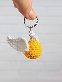 a hand holding a crocheted keychain with an angel wing on it