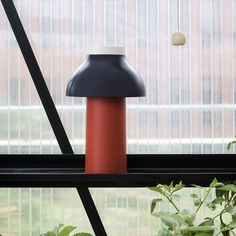 a red and black lamp sitting on top of a window sill next to a plant