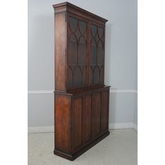 an old wooden cabinet with glass doors on the top and bottom, against a gray wall