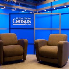 two brown chairs sitting next to each other in front of a blue wall with the united states census logo on it