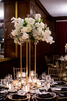 a tall vase filled with white flowers sitting on top of a table covered in candles