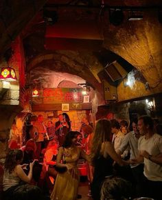 a group of people standing around in a room with lights on and some playing instruments