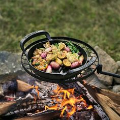 a grill with potatoes and other food cooking on top of it next to some logs