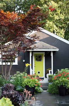 a black house with yellow door surrounded by flowers and trees