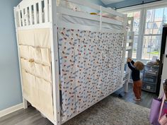 a little boy standing in front of a white crib with blue walls and curtains