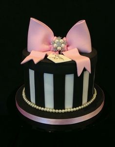 a black and white striped cake with pink bows on the top is decorated with pearls