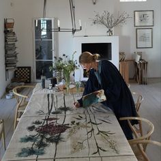 a woman is painting flowers on a table in a room with white walls and wood floors