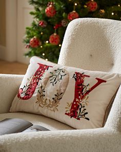 a white chair with a christmas tree in the background and a red y pillow on it