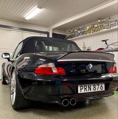 the back end of a black bmw car in a garage with other cars behind it