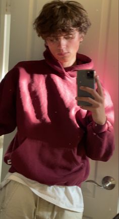 a person taking a selfie in front of a mirror wearing a red sweater and khaki pants