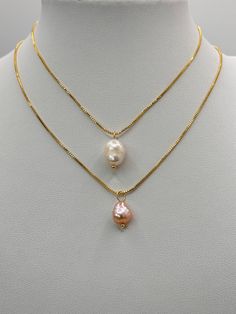 Presented here are two  gold necklace sold separately , each featuring a single baroque pearl pendant.  The  necklace length is adjustable with a sliding bead. The top chain holds a classic white pearl with a soft luster, while the second chain displays a pearl with a pinkish hue, giving off a gentle iridescence.  The baroque pearls, with their unique shapes, provide a natural and organic elegance to the otherwise sleek and simple gold plated chains. Both necklaces combine the timeless appeal of Gold Drop Necklaces With Pearl Charm, Gold Baroque Pearl Drop Necklaces, Gold Pearl Teardrop Necklace, Gold Baroque Pearl Drop Necklace, Gold Drop Baroque Pearl Necklace, Gold Adjustable Pearl Drop Necklace, Gold Pear-shaped Single Strand Pearl Necklace, Gold Teardrop Single Strand Necklace, Gold Single Strand Teardrop Necklace