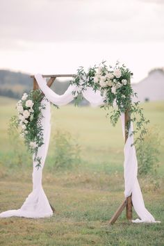 an outdoor wedding ceremony setup with white flowers and greenery on the arch, in front of a field