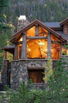 a large stone house surrounded by trees in the woods at night with lights on it's windows