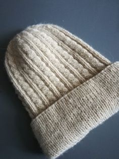 a white knitted beanie sitting on top of a blue table next to a cell phone