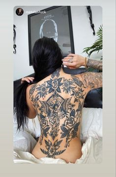 a woman with tattoos on her back sitting in bed