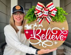 a woman holding up a sign that says believe in front of her house with christmas decorations on it