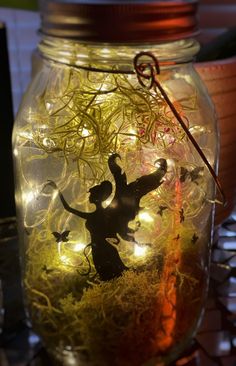 a jar filled with grass and lights on top of a table