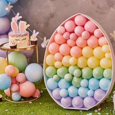 an egg shaped cake with pastel balloons in front of it