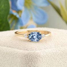 a blue ring with three diamonds sits on top of a white box next to flowers