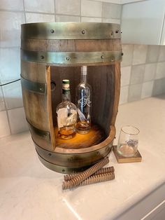 a wooden barrel with two bottles in it on top of a counter next to a glass