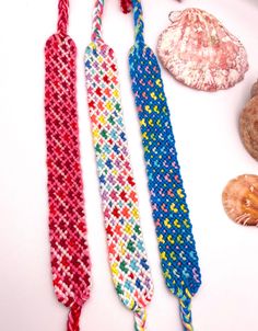 three different colored knitted ties next to seashells on a white table top