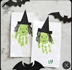 two halloween handprints on white paper with bats around them and one has a black witch's hat